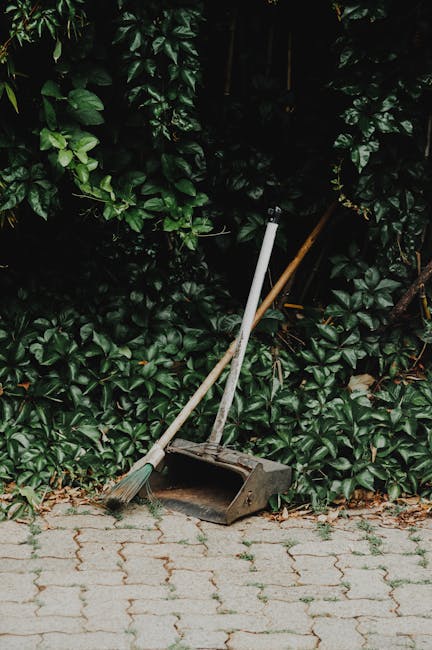 An outdoor scene depicting a pile of discarded household items and debris on a paved surface. The clutter includes a wooden garden chair with slatted backrest and frame, placed at an angle on the left